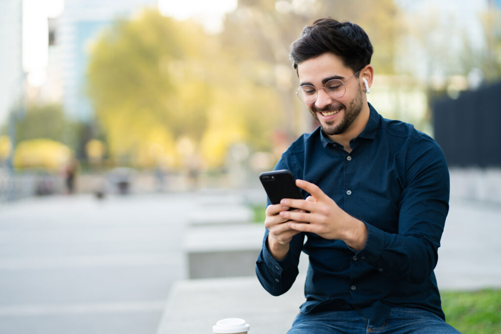 homem sorrindo utilizando o celular e fones de ouvido