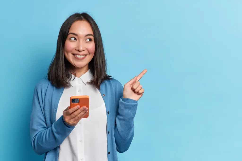 mulher feliz segurando o celular e apontando com o dedo para cima