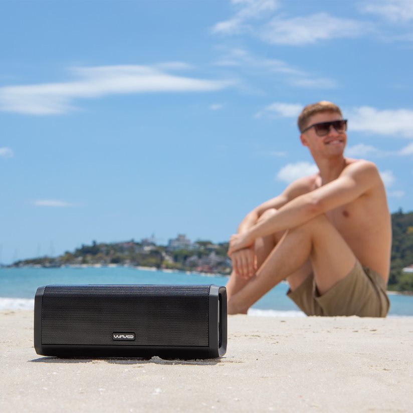 Homem na praia escutando uma caixa de som bluetooth na areia da WaveOn