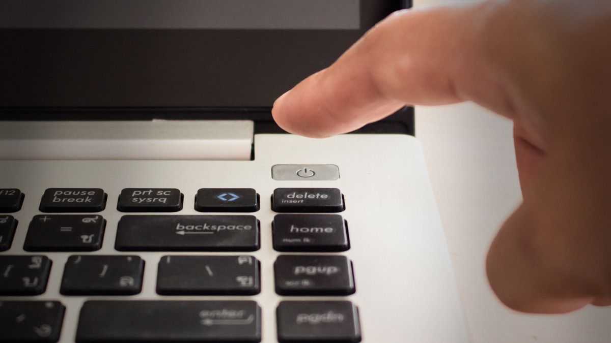 Um dedo prestes a pressionar o botão liga/desliga de um laptop.
